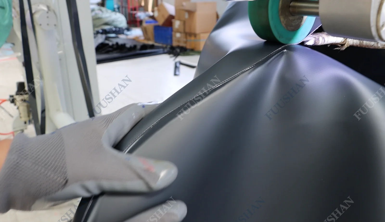 Gloved hand guiding dark fabric beneath a welding machine roller